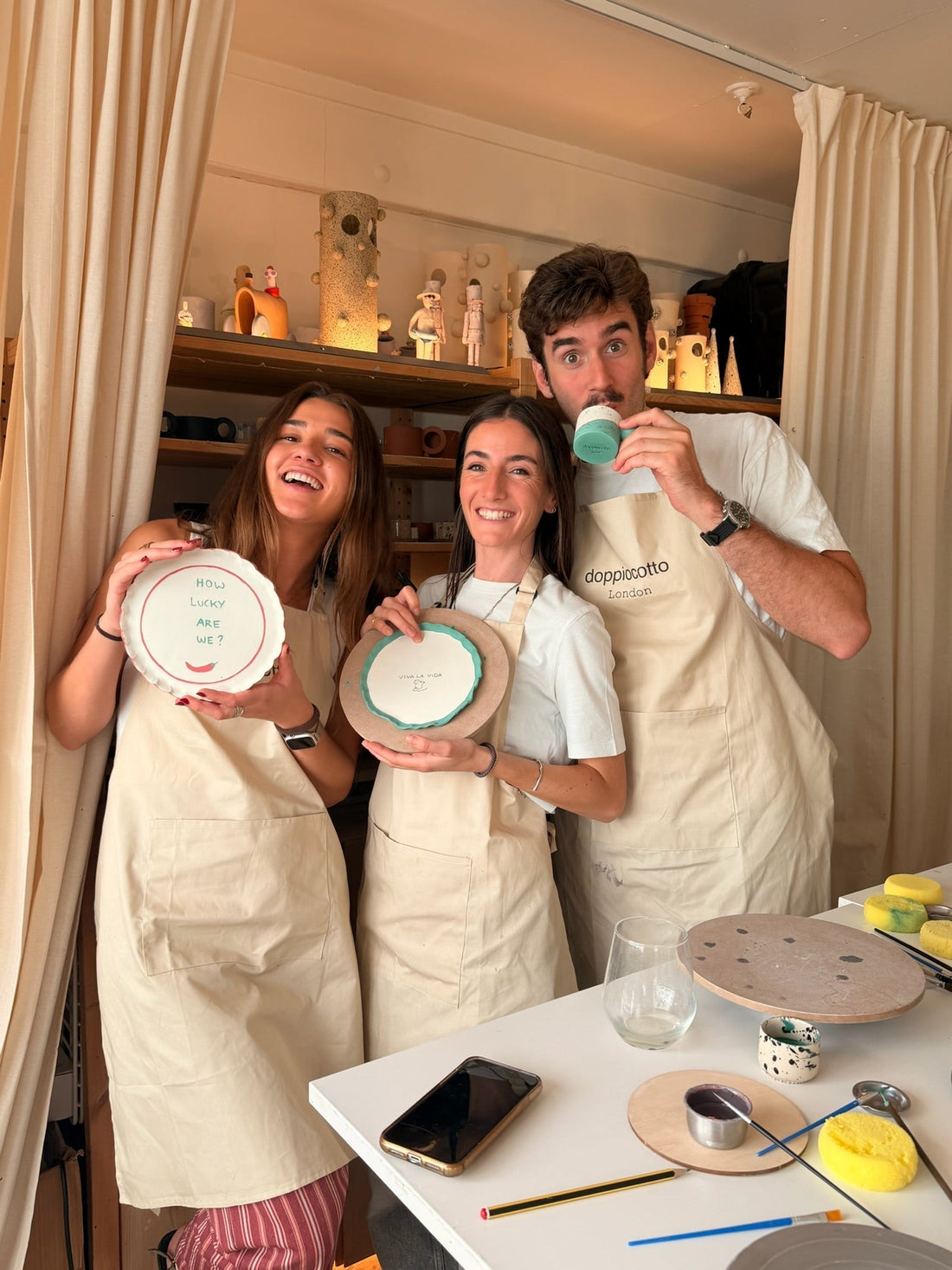 Friends laughing while holding hand-painted ceramic plates at a pottery at birthday party in London, Doppiocotto studio