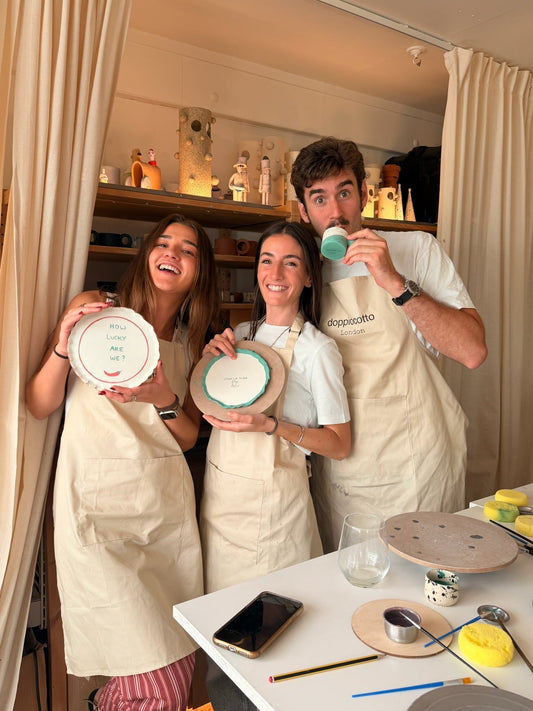 Friends laughing while holding hand-painted ceramic plates at a pottery at birthday party in London, Doppiocotto studio