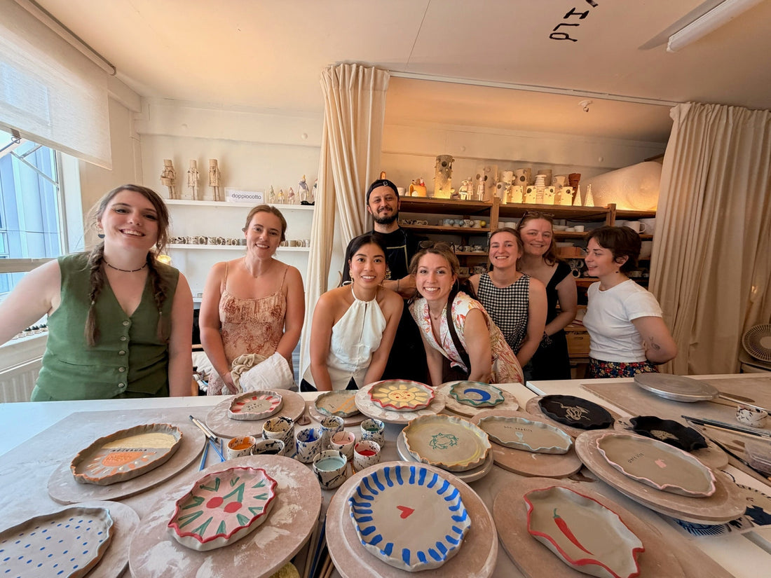 Friends laughing while holding hand-painted ceramic plates at a pottery hen party in London, Doppiocotto studio