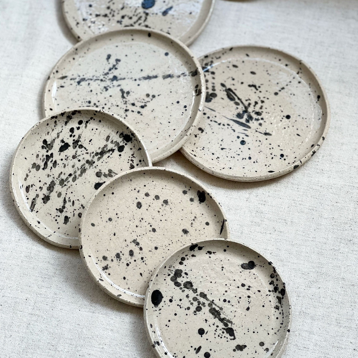 Black stoneware saucer with splashed design, 15 cm diameter, by doppiocotto, displayed on a neutral background.